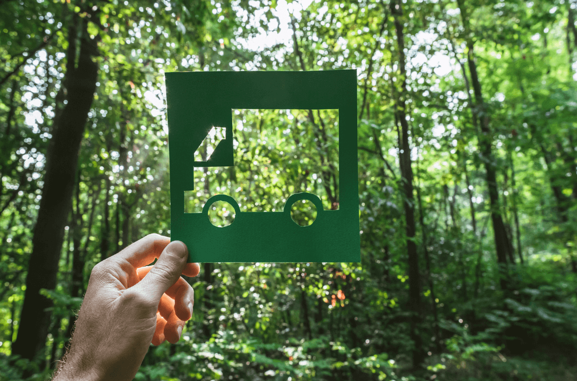 Paper cut-out truck against a forest backdrop highlighting environmental impact in logistics.