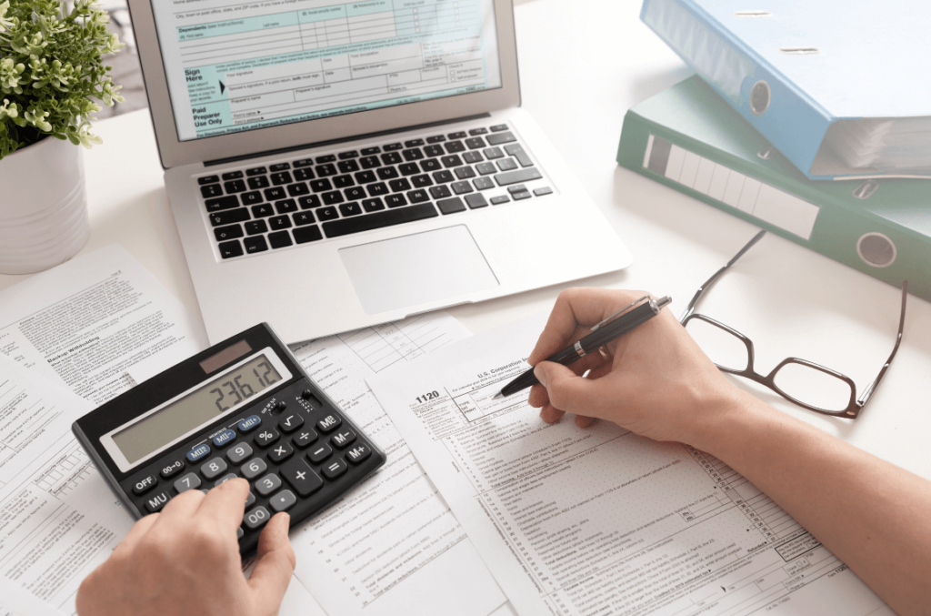 Individual using a calculator and laptop to determine tax implications for shipments
